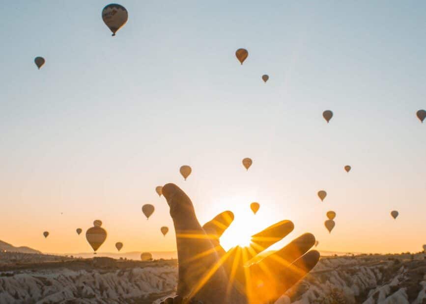 photo of person s hand across flying hot air balloons during golden hour