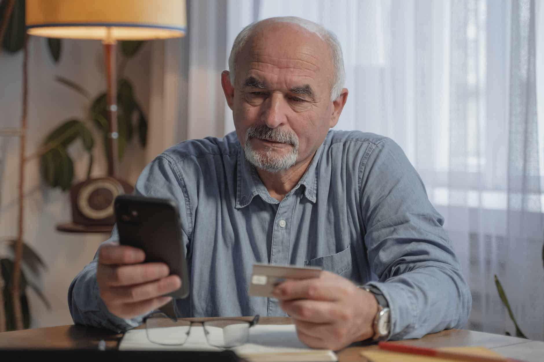 an elderly man holding his mobile phone and a credit card