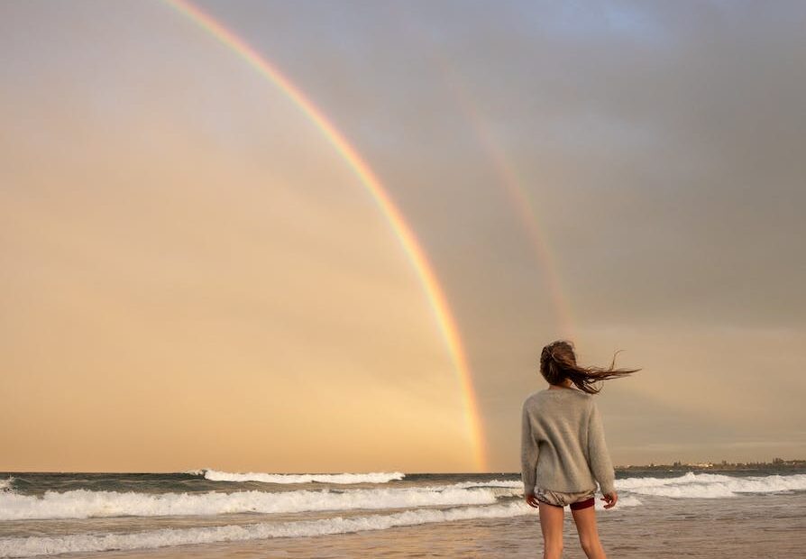 unrecognizable woman standing on shore with rainbow