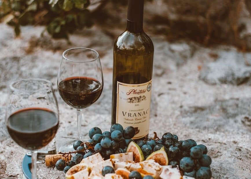 glasses of wine beside grapes and wine bottle on gray ground