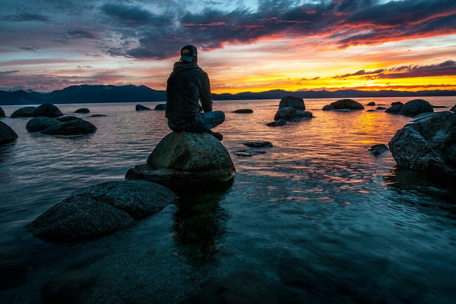 person sitting on rock on body of water