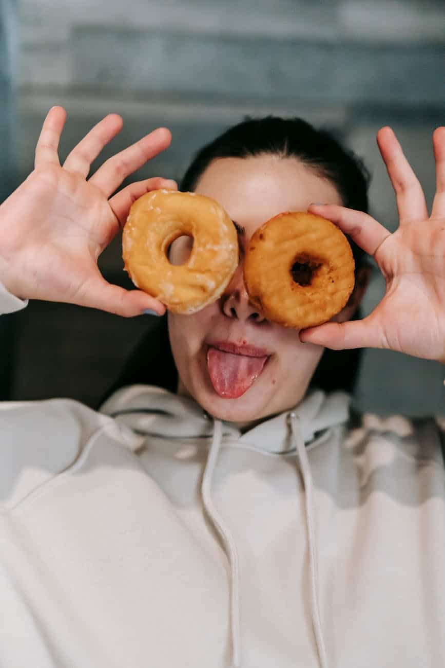 joyful woman covering eyes with donuts and showing tongue